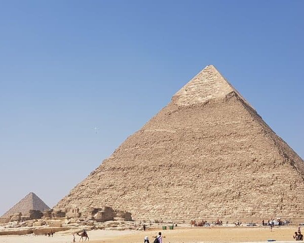 Tourists standing in front of the Great Pyramids and the Sphinx.